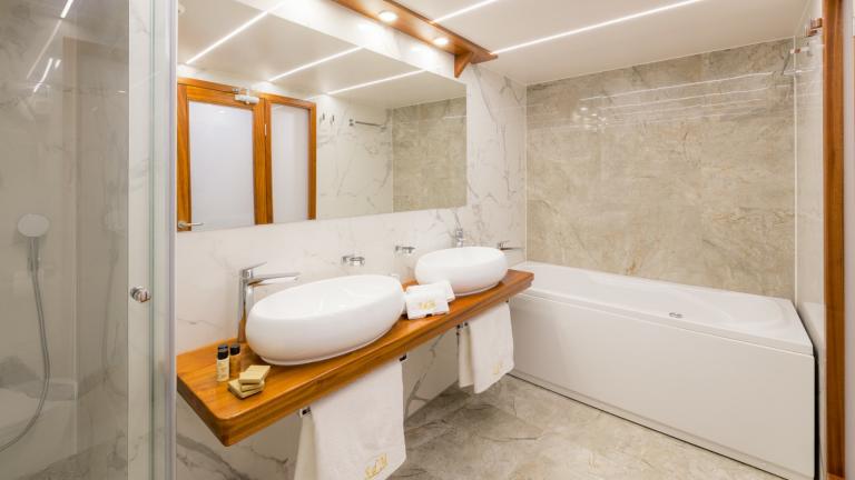 Ein edles Badezimmer aus hellem Marmor mit einer Badewanne und zwei Designer Waschschüsseln.